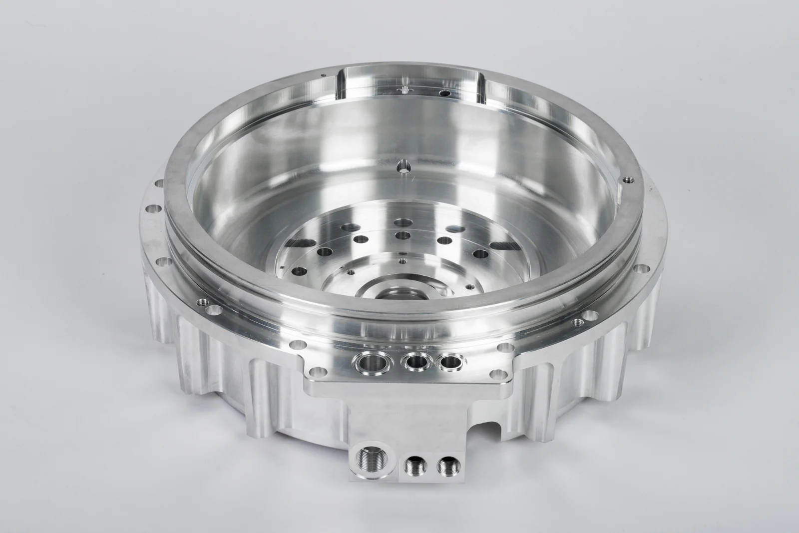 Silver-colored circular metal housing with a machined cavity, mounting holes and a flanged rim.